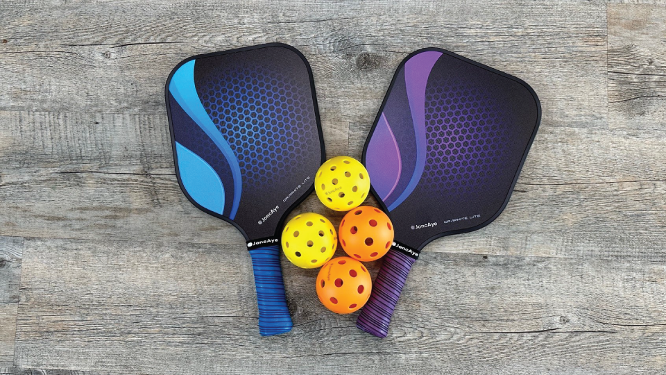 Two pickle ball paddles with two yellow balls and two orange balls