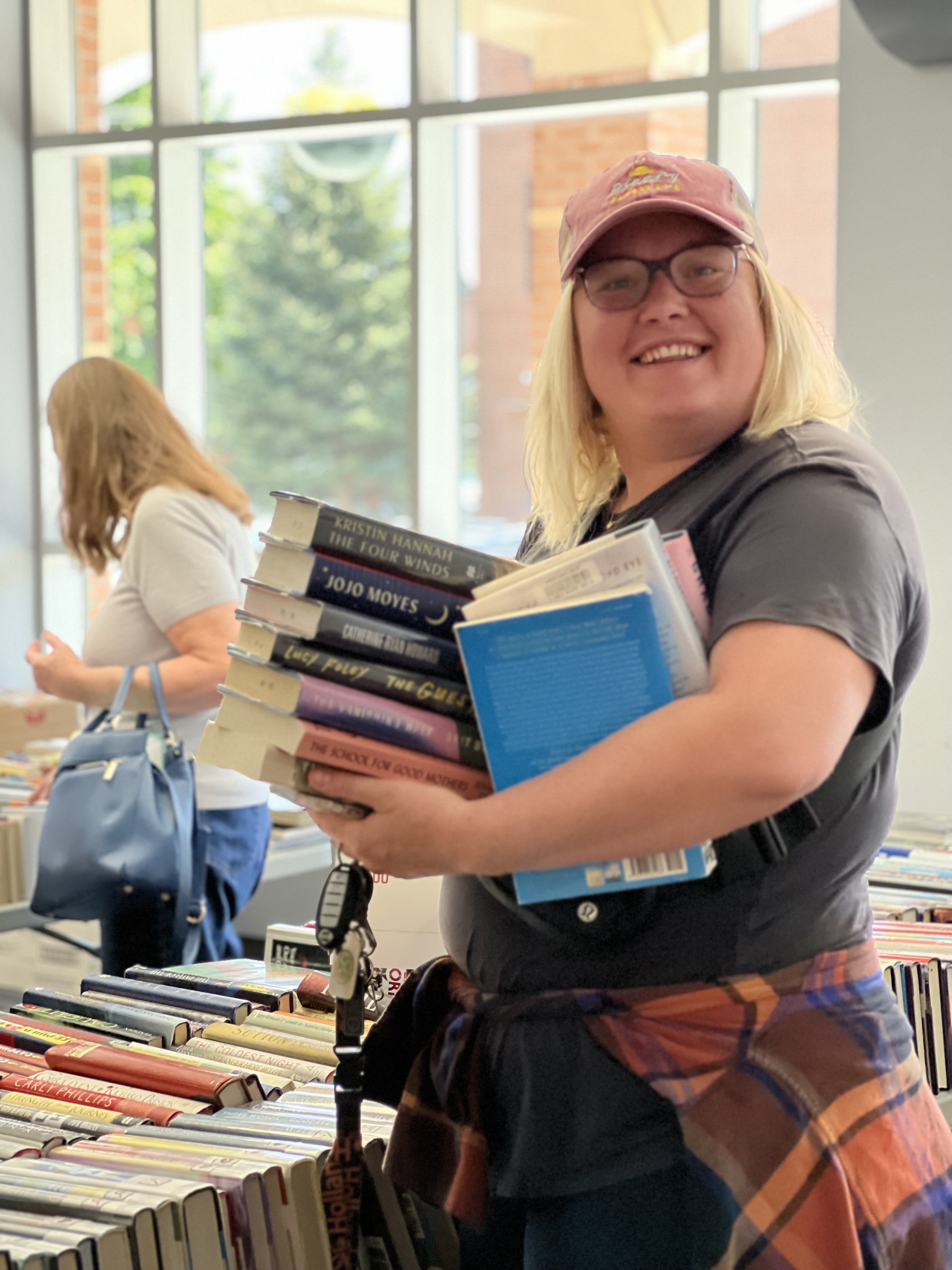 A woman at the book sale holding a large stack of books, smiling at the camera.
